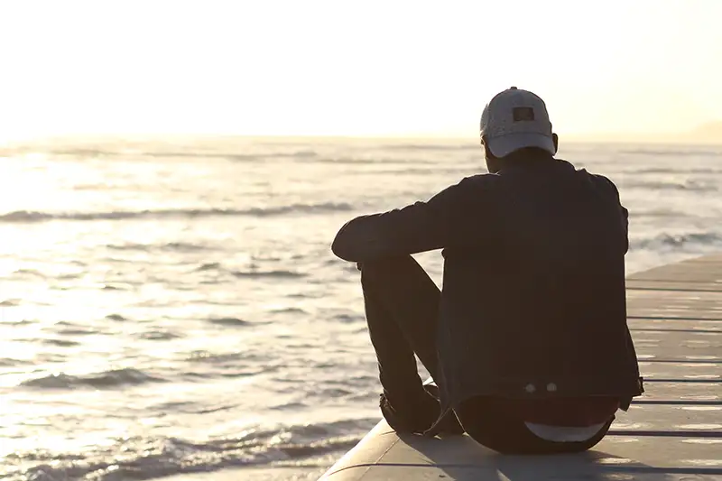 Ein Mann mit Basecap sitzt am Meer und macht sich Gedanken ob er nach Kalabrien auswandern will